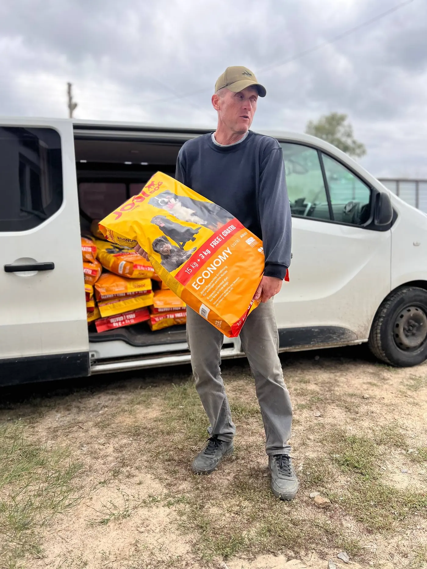 A man carrying an 18 kg bag of Josera YoziDog Economy from a white van stacked with more bags