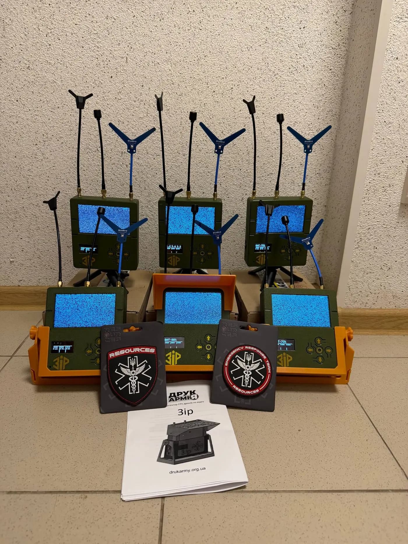 Six ZIR drone detectors with their antennas in two rows on a tiled floor, two Resources ERT patches and the maker's manual in front